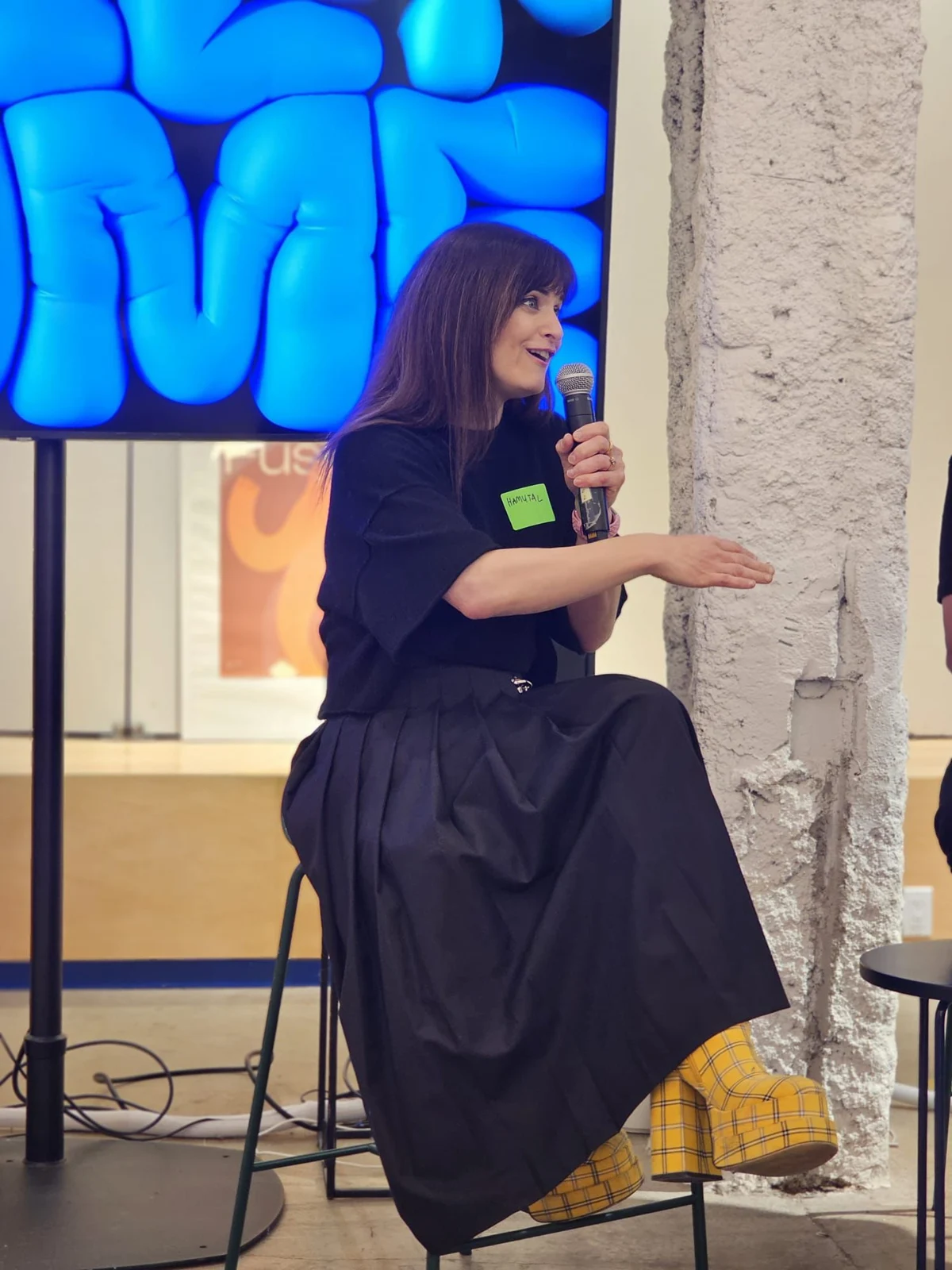 Hamutal Schieber speaking at Bereisheet Tech, seated in yellow boots